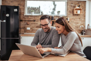 Young spouses sitting at the table in their homely apartment and looking at laptop.